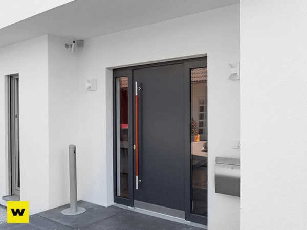 Moderne Haustür aus Aluminium mit großem Griff und Seitenteil an weißer Hausfassade.