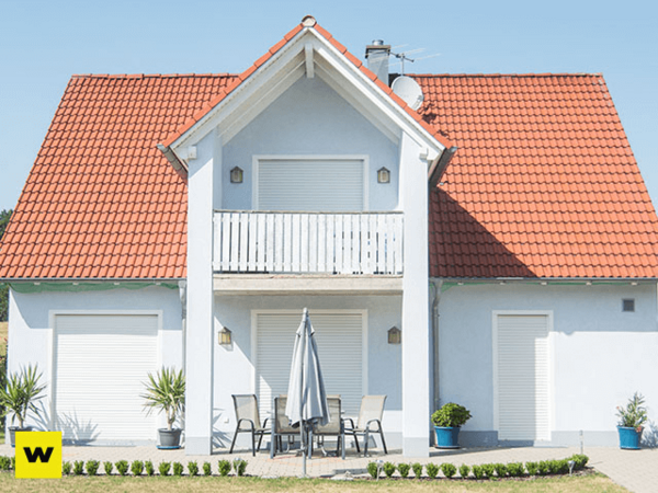 Modernes Einfamilienhaus mit rotem Satteldach, Terrasse und Rollläden an Fenstern.